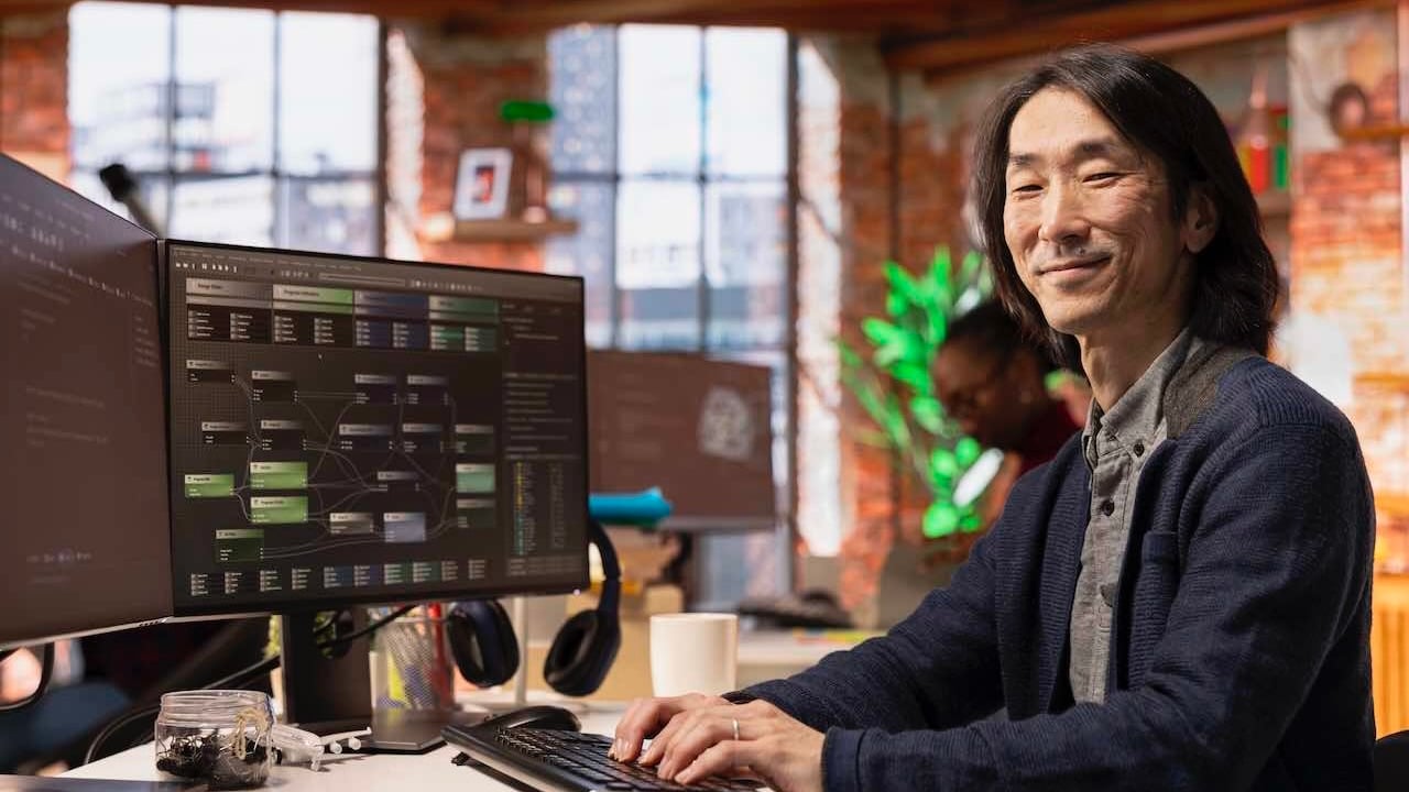 Người đang làm việc tại bàn với hai màn hình hiển thị giao diện phần mềm. 